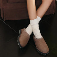 Brown suede shoes worn with white socks on a dark floor.