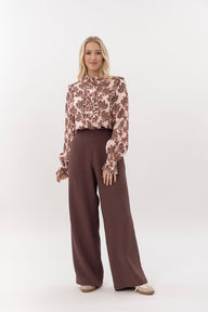Woman wearing a floral blouse and brown wide-leg pants on a white background