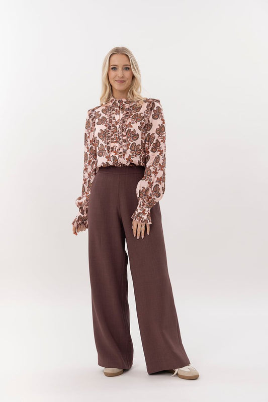 Woman wearing a floral blouse and brown wide-leg pants on a white background