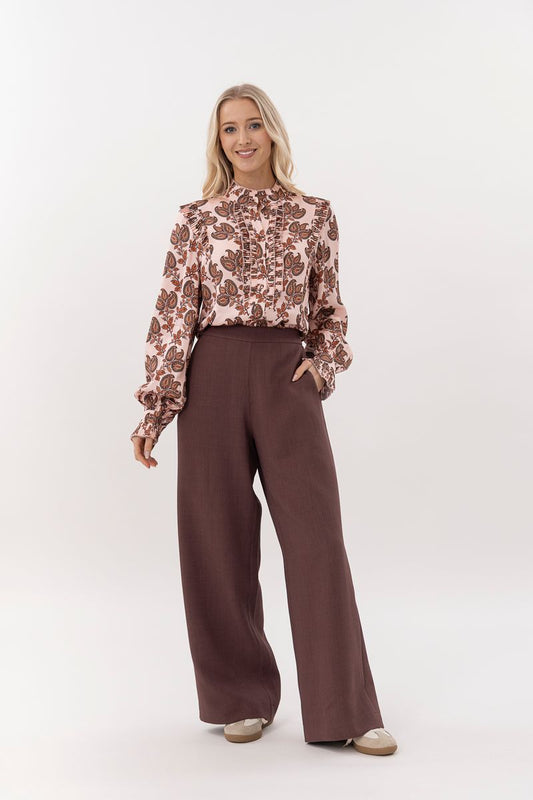 Woman wearing a patterned blouse and brown wide-leg pants on a white background
