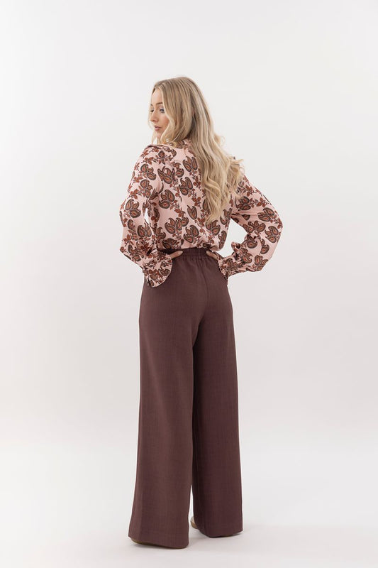 Woman wearing a floral blouse and brown pants on a white background
