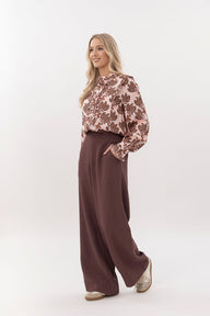 Woman wearing a floral blouse and brown wide-leg pants on a white background