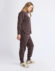 Woman wearing a brown tracksuit with white sneakers on a light gray background