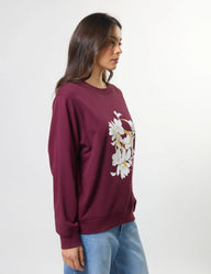 Woman wearing a maroon sweatshirt with floral design on a white background