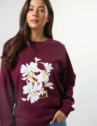 Woman wearing a maroon sweatshirt with floral design on a plain background