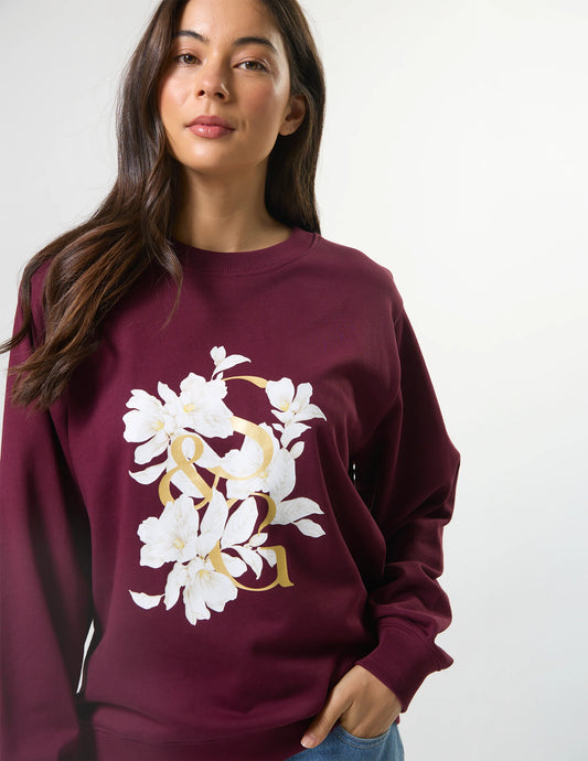 Woman wearing a maroon sweatshirt with floral design on a plain background