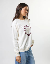 Woman wearing a white sweatshirt with text, standing against a plain background
