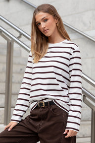 Woman wearing a striped long-sleeve shirt and brown pants against a neutral background