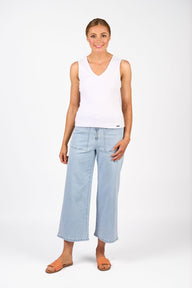 Woman wearing a white sleeveless top and light blue jeans on a white background