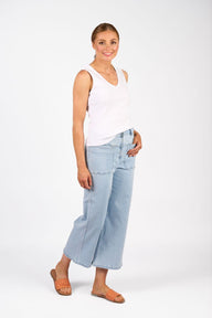 Woman wearing a white sleeveless top and light blue jeans on a white background