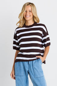Woman wearing a chocolate and white striped sweater and blue jeans on a plain background