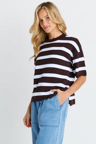 Woman wearing a brown and white striped sweater with blue jeans on a white background