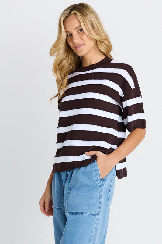 Woman wearing a brown and white striped sweater with blue jeans on a white background