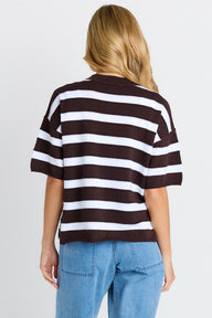 Person wearing a brown and white striped shirt with blue jeans on a plain background