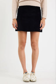 Person wearing a black mini skirt with a beige sweater and white sneakers on a plain background