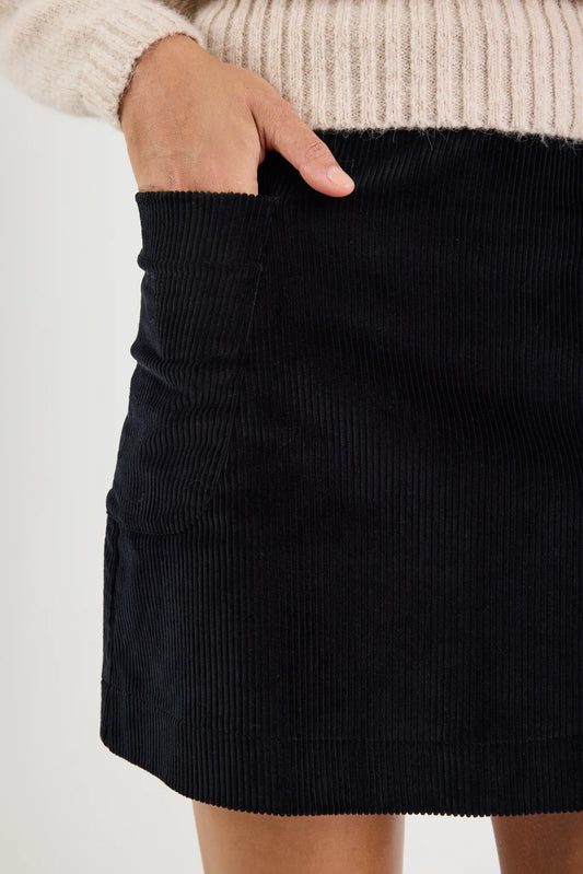 Black corduroy skirt worn with a beige sweater on a white background