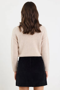 Person wearing a beige sweater and black skirt on a white background
