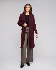 Woman wearing a long burgundy cardigan over a black top and gray pants on a white background