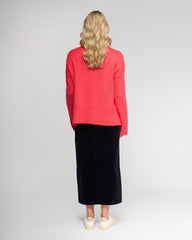 Person wearing a coral sweater and black skirt on a white background