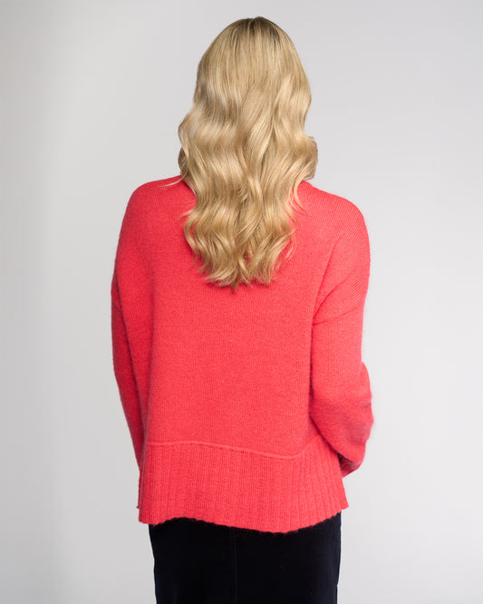 Person wearing a coral sweater with a plain background