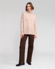 Woman wearing a oat sweater and brown pants on a white background