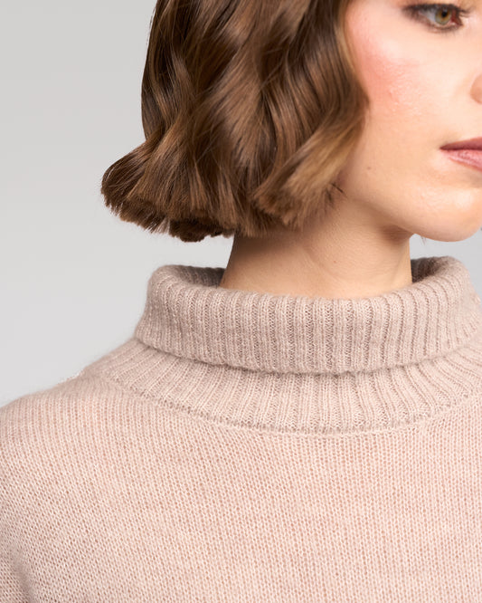 Close-up of a person wearing a oat turtleneck sweater with a neutral background
