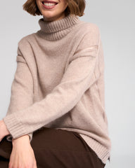 Person wearing a oat turtleneck sweater against a plain background