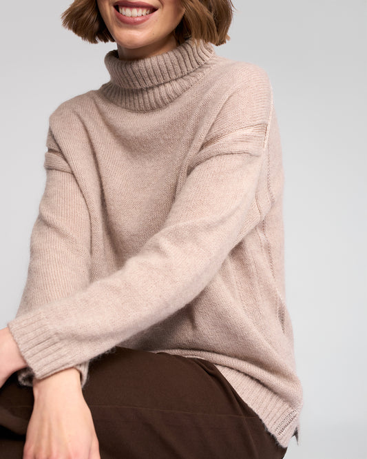 Person wearing a oat turtleneck sweater against a plain background
