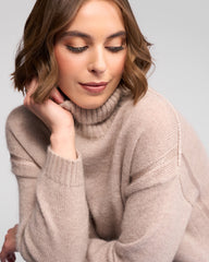 Woman wearing a oat turtleneck sweater against a light gray background
