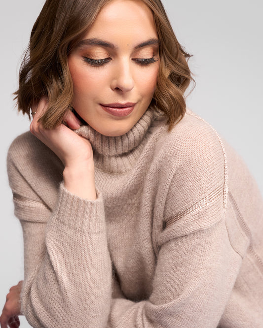 Woman wearing a oat turtleneck sweater against a light gray background