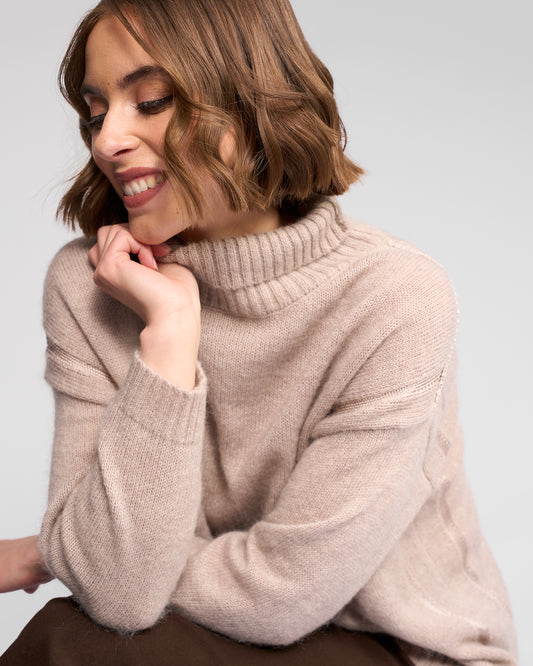 Woman wearing a oat turtleneck sweater against a light gray background