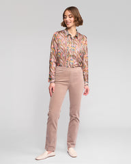 Woman wearing a patterned blouse and beige pants on a plain background