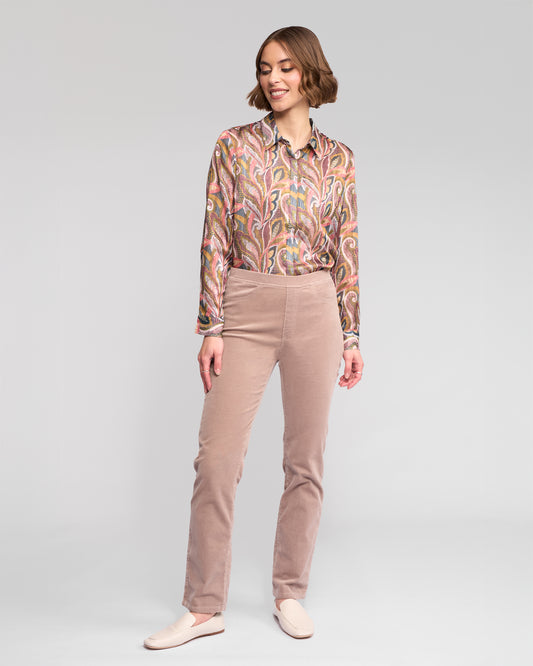 Woman wearing a patterned blouse and beige pants on a plain background