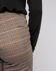 Houndstooth patterned pants with a black long-sleeve shirt on a light gray background