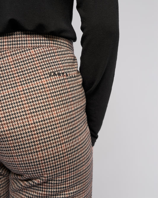 Houndstooth patterned pants with a black long-sleeve shirt on a light gray background