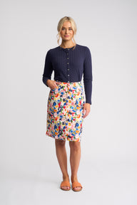 A woman modeling a navy blue ribbed long-sleeve top and a knee-length white skirt with a colorful abstract floral print, standing against a light gray studio background.