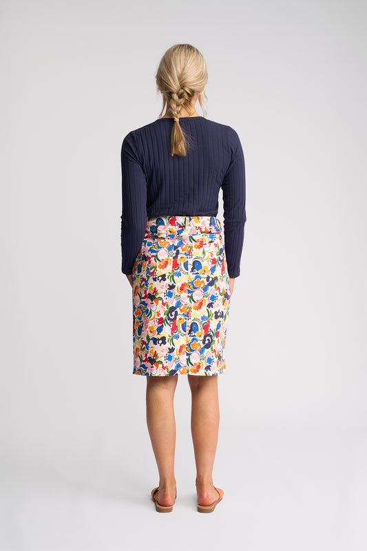 A woman viewed from the back wearing a navy ribbed long-sleeve top and a knee-length skirt with a colorful abstract pattern, standing against a light gray studio background.