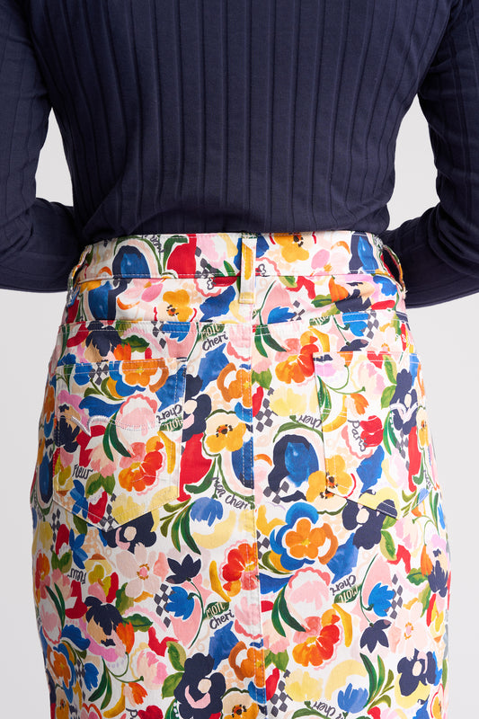 A close-up of a person wearing a colorful floral print skirt with a white waistband and belt, paired with a dark navy ribbed long-sleeve top. The skirt features a busy pattern of flowers and text including 'Sunny Days' and 'Enjoy the Day'.