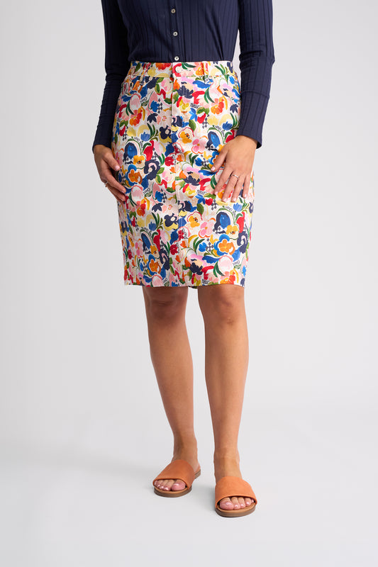A model wearing a colorful floral print pencil skirt with a navy blue long-sleeve top and tan slide sandals, shown from the waist down against a light gray studio background.