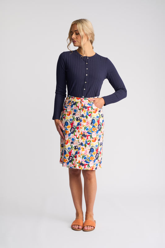 A woman modeling a navy blue ribbed long-sleeve top and a colorful, patterned knee-length skirt against a light gray studio background.