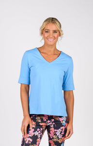 Woman wearing Vassalli light blue top and colorful patterned pants on a white background