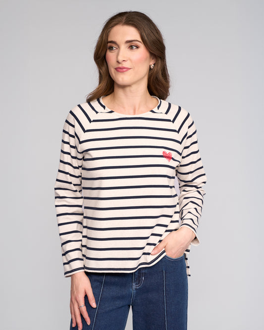 Woman wearing a oat and ink striped long-sleeve shirt with a red logo on a gray background