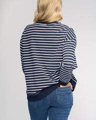 Person wearing a navy and white striped shirt with blue jeans on a gray background