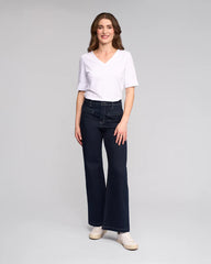 Woman wearing a white top and dark jeans on a gray background