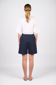 Woman wearing a white blouse and Vassalli Pleat detail navy shorts on a white background