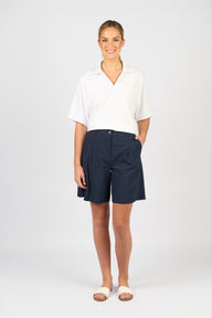 Woman wearing a white blouse and Vassalli Pleat detail navy shorts on a white background