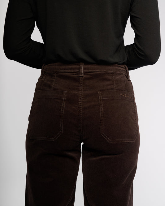 Person wearing brown corduroy pants and a black long-sleeve shirt on a white background